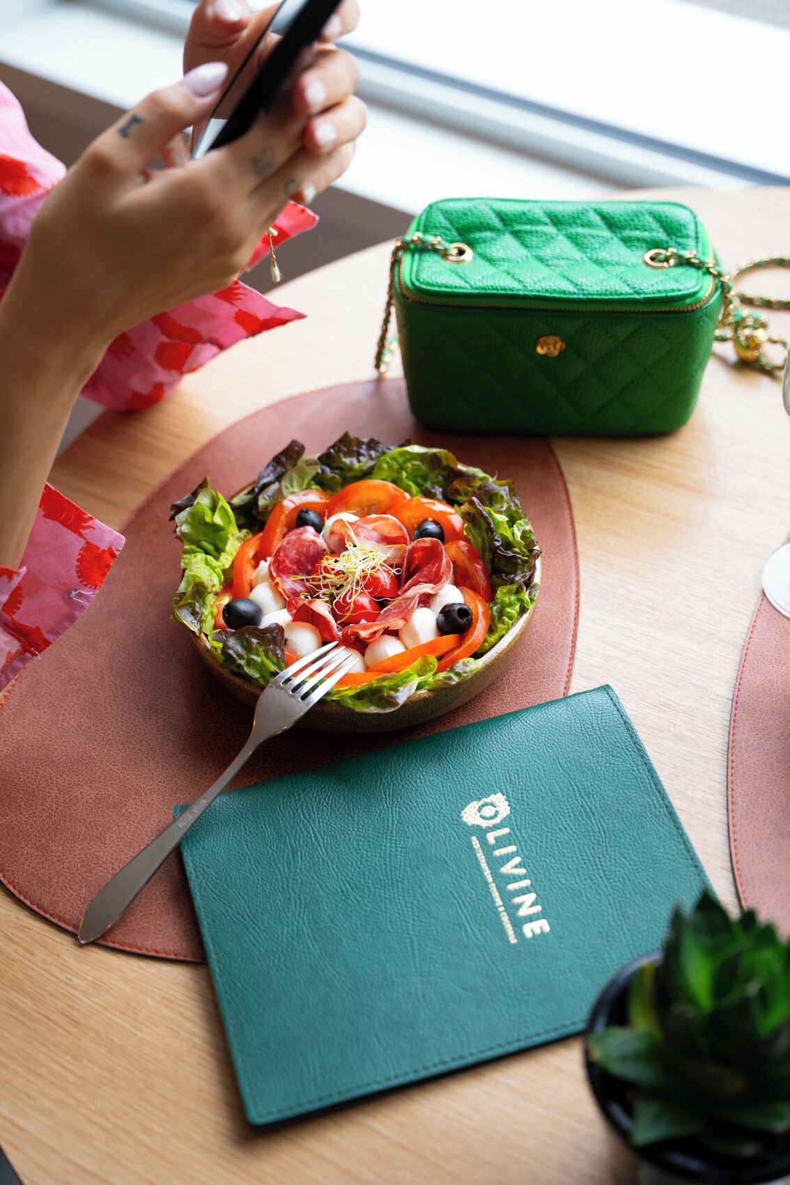 A salad on a wooden table with a green wallet and a notebook.