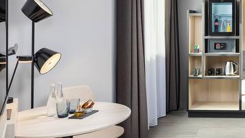 A modern hotel room with a round dining table, two chairs, a floor lamp, a minibar, and a large window with curtains.