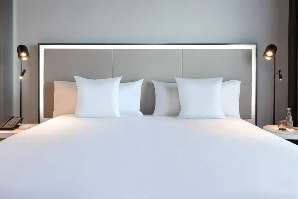 Un lit bien fait, avec du linge de lit blanc et une tête de lit dotée d’un éclairage intégré.