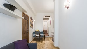 A hallway with a herringbone floor, a sofa with a purple cushion, a wooden door, and a dining area with a table and chairs. - Casa Tina (Florence)
