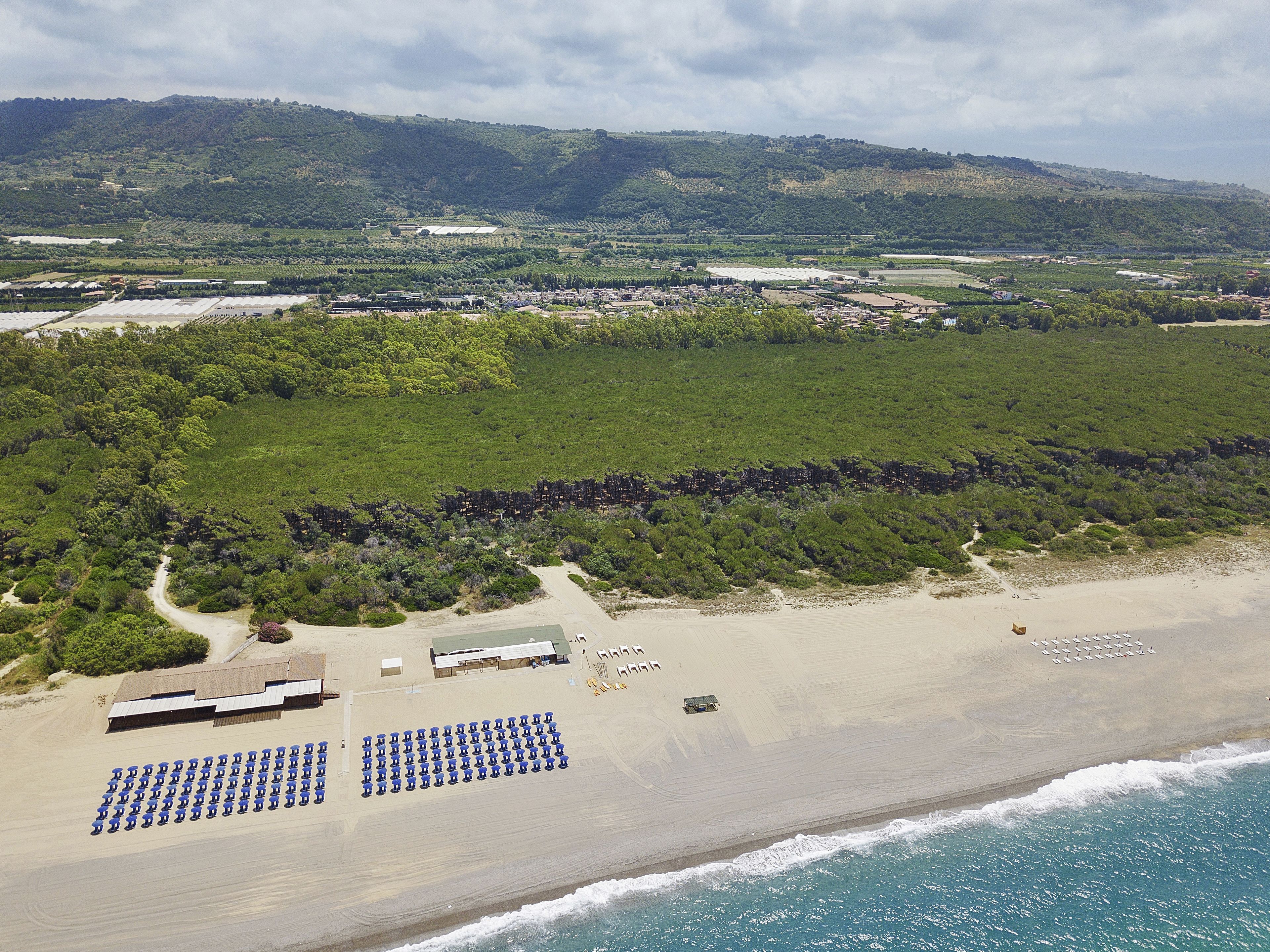 An aerial view of a beach with rows of blue chairs, a sandy beach, and a hilly landscape in the background.