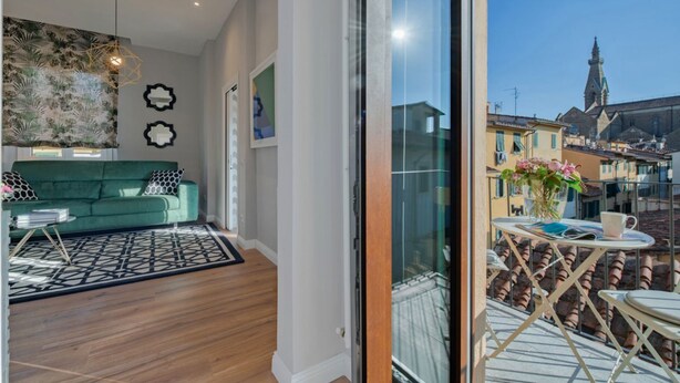 Un salon moderne avec un canapé vert, un tapis à motifs géométriques et une vue sur la ville, visible à travers une porte vitrée.