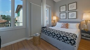 Une chambre à coucher avec un lit, des lampes de chevet, une fenêtre, un radiateur et des œuvres d’art accrochées au mur.