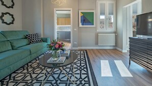 Un salon moderne avec un canapé vert, une table basse agrémentée de livres et de fleurs, un tapis à motifs géométriques et un grand téléviseur posé sur un meuble en bois.