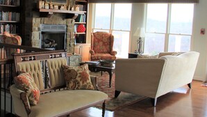 A spacious living room with a fireplace, bookshelves, a comfortable armchair, and a sofa. - Inn at Riverbend (Pearisburg)