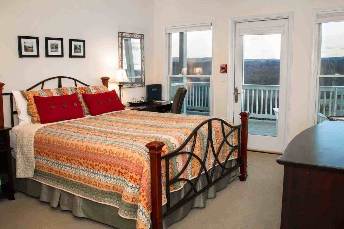 A bedroom with a bed, a nightstand, a dresser, a mirror, and a window with a view.