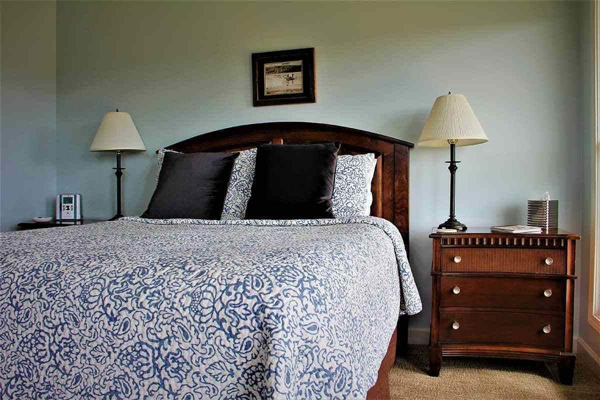 A bedroom with a large bed, two bedside tables, a nightstand, a framed picture on the wall, and a lamp on each bedside table.
