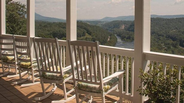 A porch with white rocking chairs and a view of a river and forested hills. - Inn at Riverbend (Pearisburg)