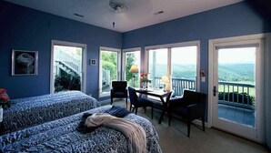 A bedroom with two beds, a dining table, and chairs. There are large windows with a view of the outdoors. - Inn at Riverbend (Pearisburg)