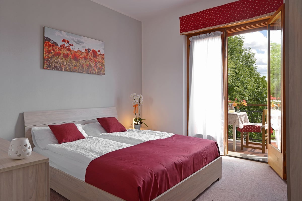 A modern bedroom with a large bed, a potted orchid, and a view of a balcony with outdoor seating.