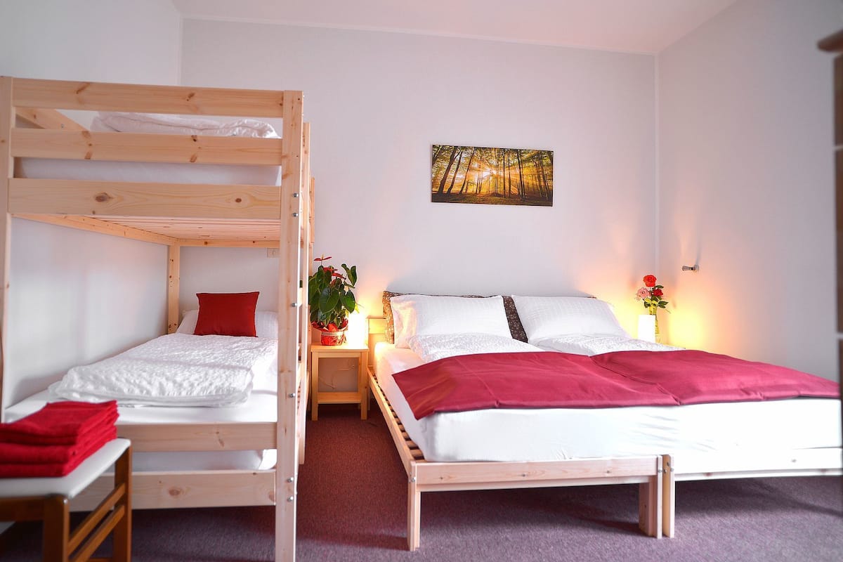 A room with a bunk bed, a single bed, a bedside table with a lamp, and a painting on the wall.