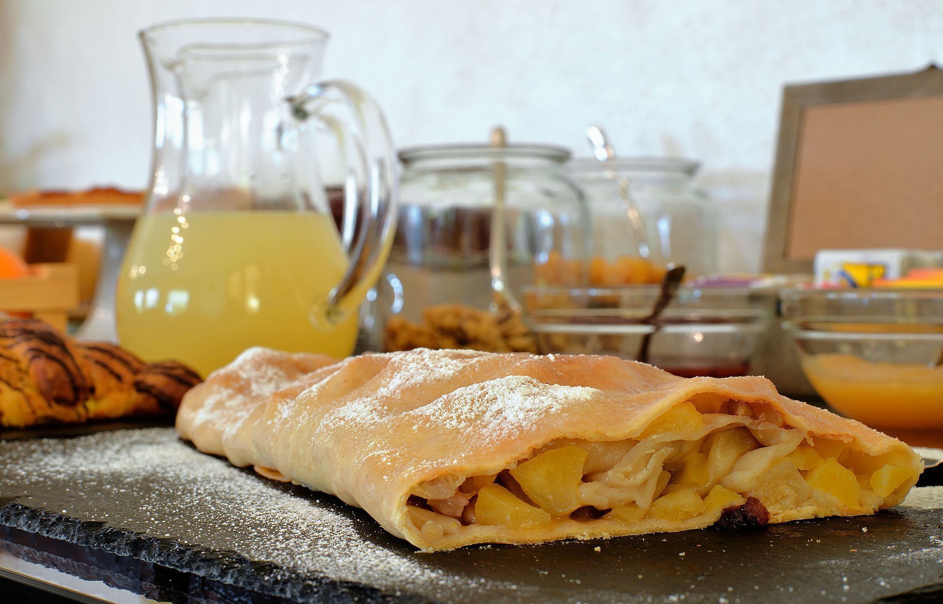 A dessert with a flaky crust, possibly a pastry, on a slate serving tray.