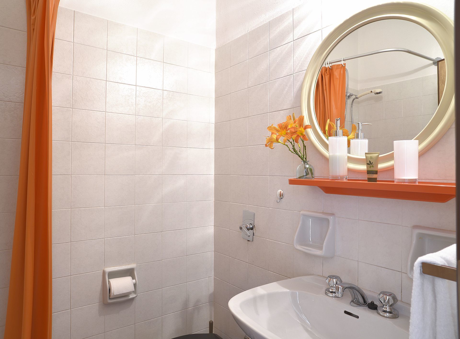 A bathroom with a shower, a sink, a mirror, and toiletries.