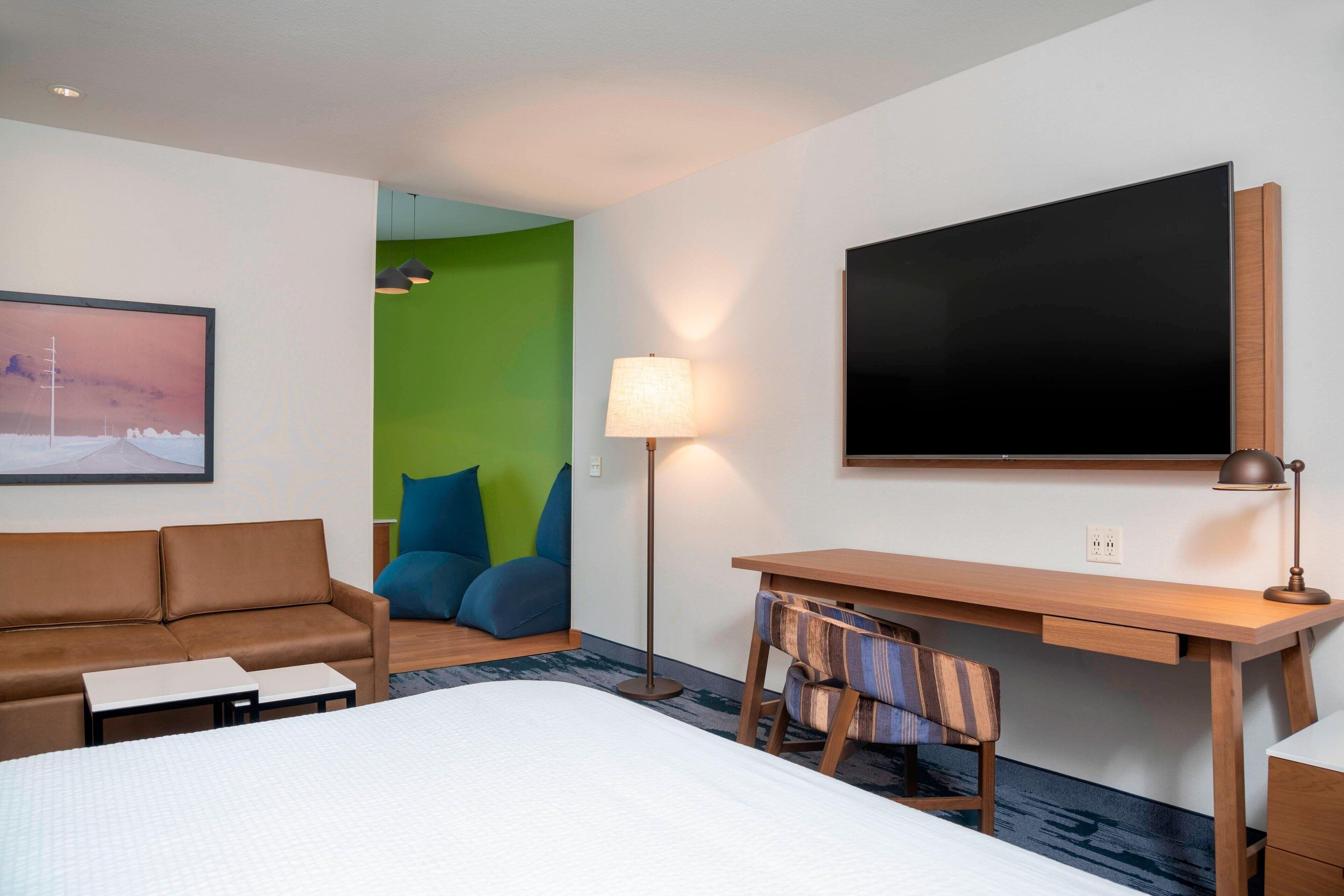 Una camera d'albergo con un letto, una scrivania con una sedia, un divano, una lampada e un quadro appeso al muro.