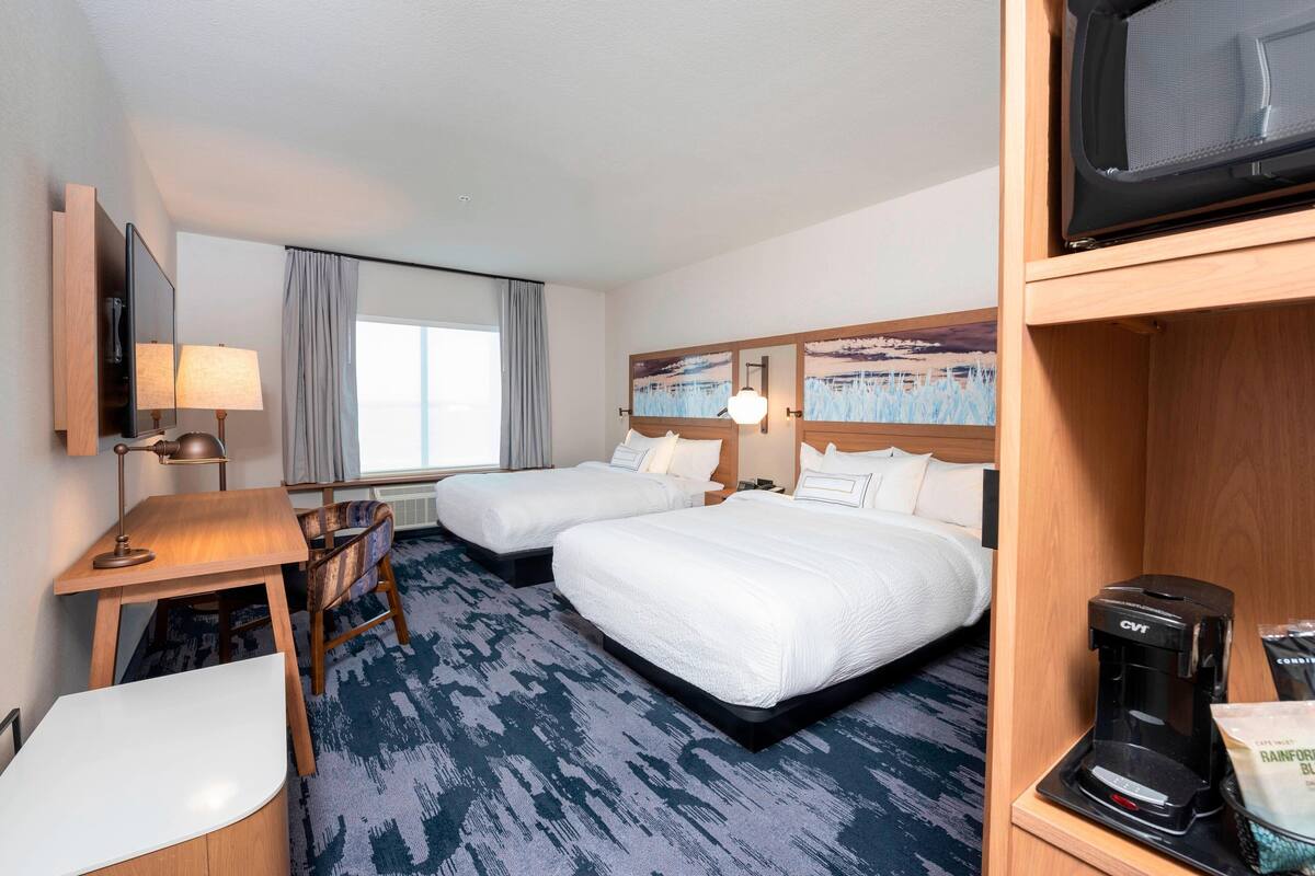Une chambre d’hôtel avec deux lits, un bureau avec une chaise, une télévision et une machine à café.