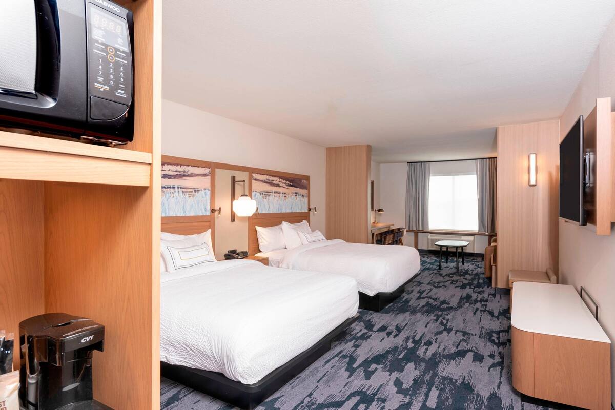 Une chambre d’hôtel avec deux lits, une télévision, une machine à café et un bureau avec une chaise.