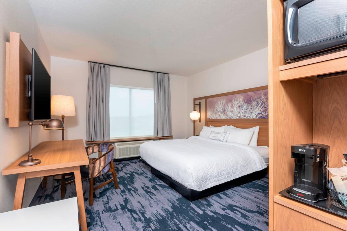 Une chambre d’hôtel équipée d’un lit, d’un bureau avec une lampe, d’une télévision et d’une machine à café.