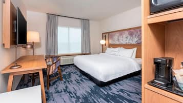 A hotel room with a bed, a desk with a lamp, a television, and a coffee maker.