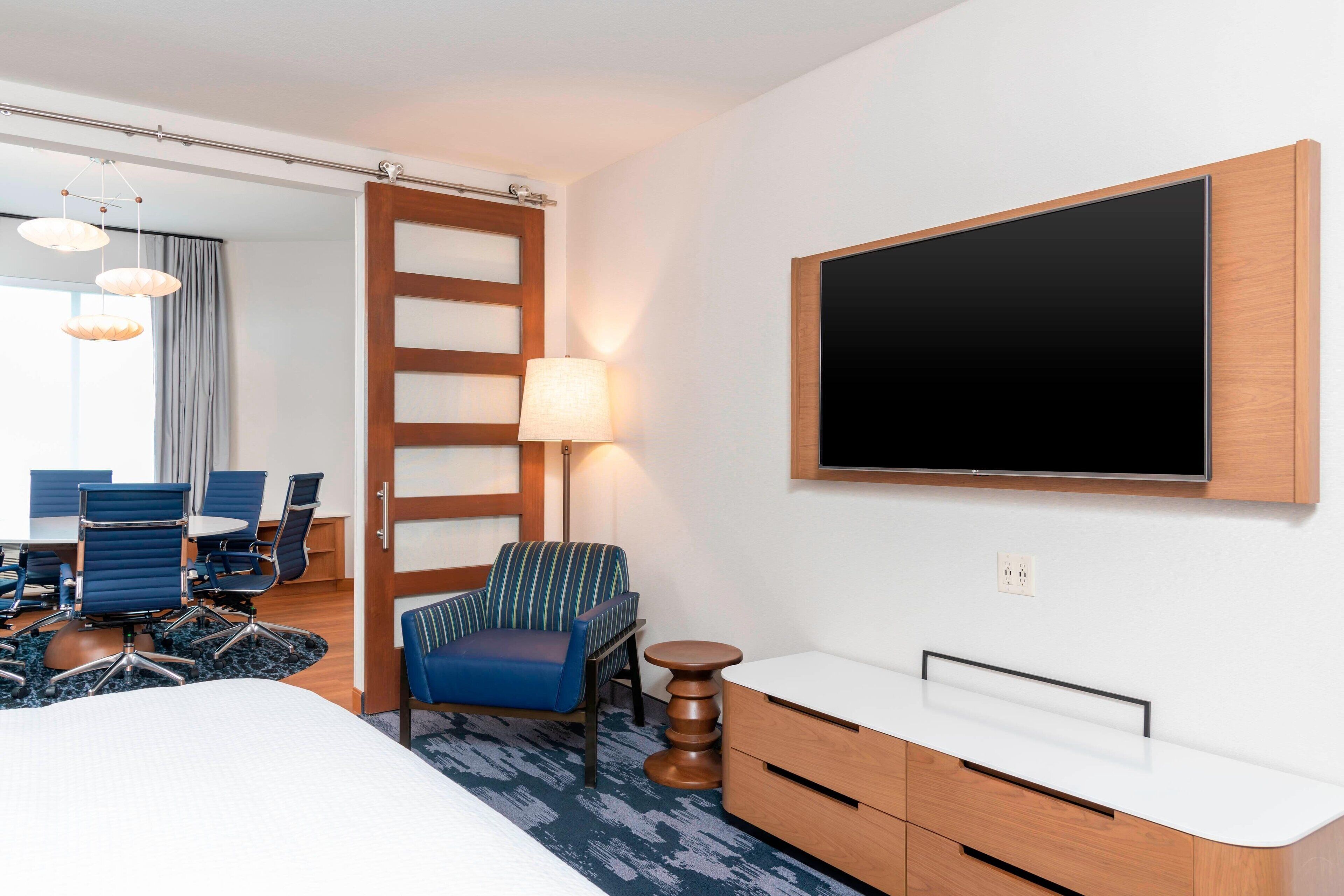 Una habitación de hotel con cama, escritorio, silla, televisor y lámpara.