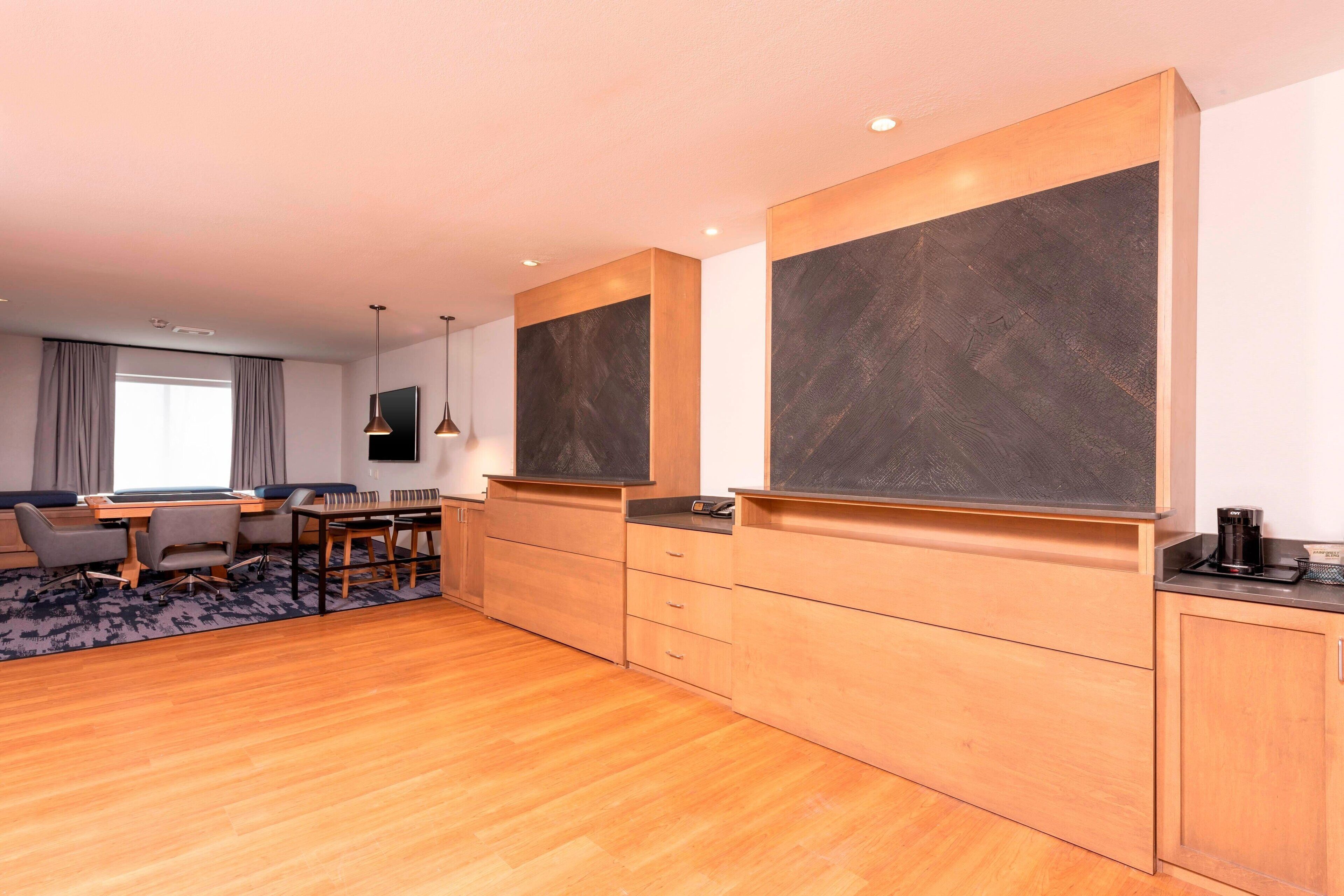 A modern hotel room with a wooden floor, a dining area with a table and chairs, a large flat-screen TV, and built-in cabinets.