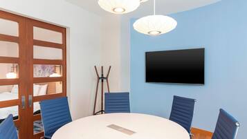 A conference room with a round table, four blue chairs, a flat-screen TV on the wall, and a wooden door with glass panels.