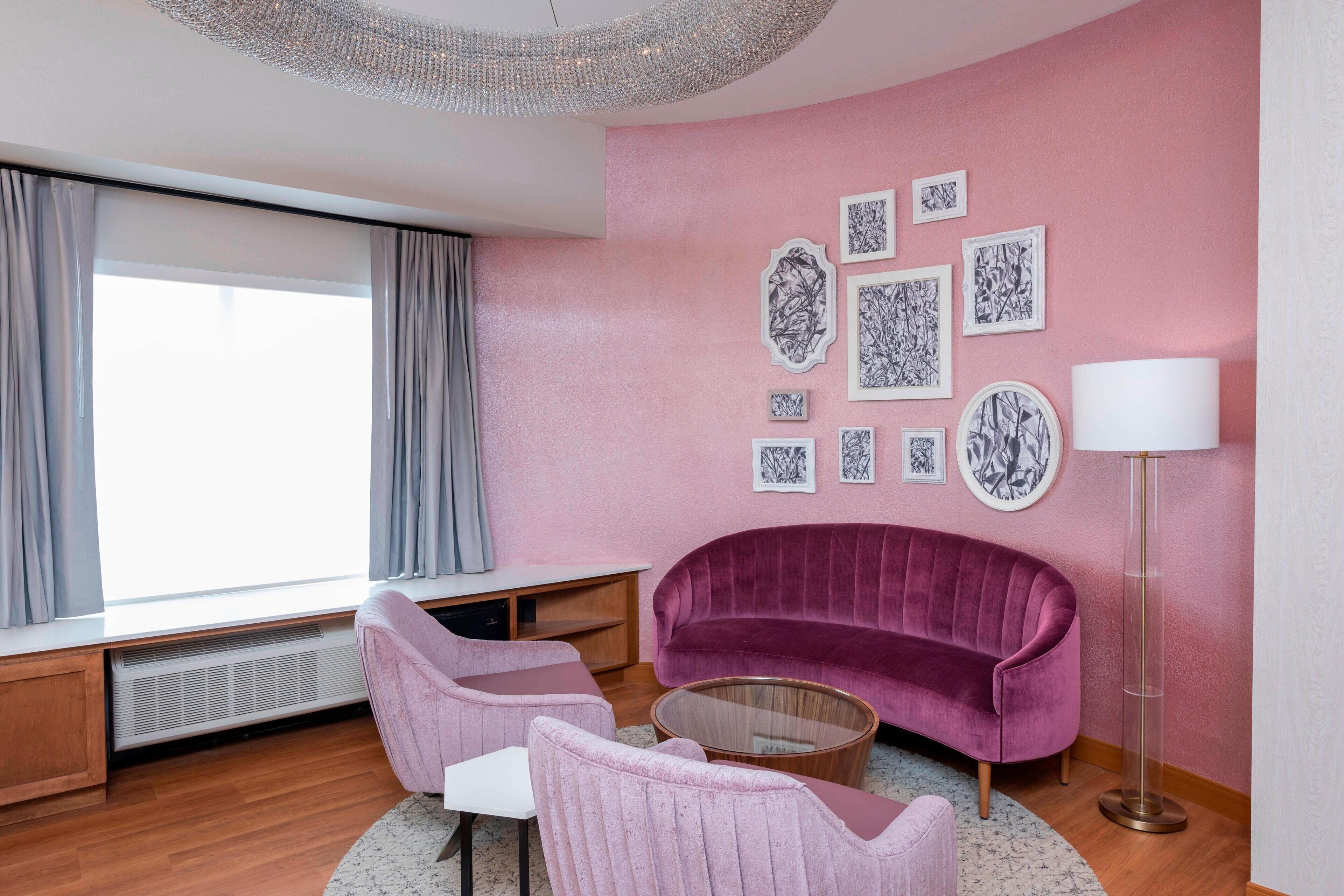 A modern living room with a pink wall, a purple sofa, two pink chairs, a coffee table, and a floor lamp.