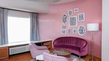A modern living room with a pink wall, a purple sofa, two pink chairs, a coffee table, and a floor lamp.