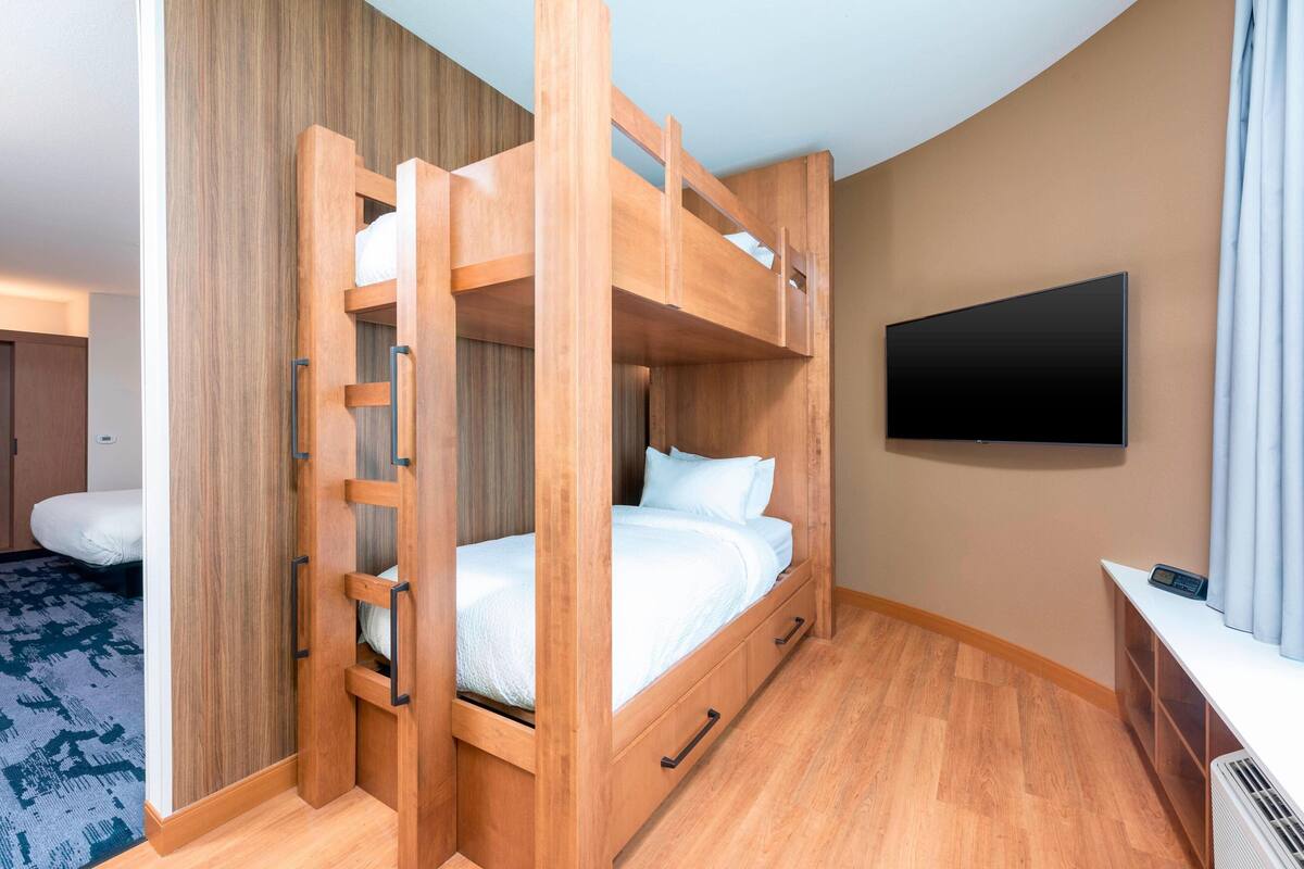 Une chambre avec des lits superposés, un téléviseur fixé au mur, un plancher en bois et une moquette à motifs.