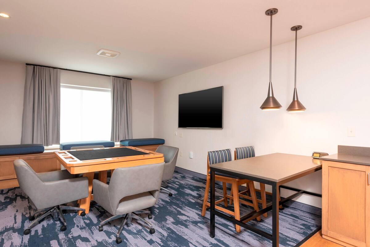 Une chambre d’hôtel avec un grand lit, un bureau avec une chaise, une petite table avec deux chaises, un téléviseur fixé au mur et deux lampes suspendues.