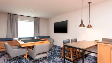 Habitación de hotel con una cama grande, un escritorio con silla, una mesita con dos sillas, un televisor montado en la pared y dos lámparas colgantes.