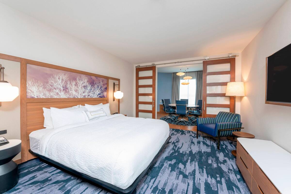 Une chambre d’hôtel avec un grand lit, un bureau avec une lampe, une chaise, un canapé et un grand miroir.