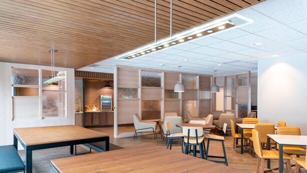 Een modern interieur met houten tafels en stoelen, een keukenhoek en een zithoek met een witte muur en planken.