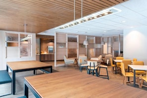 A modern interior with wooden tables and chairs, a kitchen area, and a seating area with a white wall and shelves. - Fairfield Inn & Suites by Marriott Fair Oaks Farms (Fair Oaks)