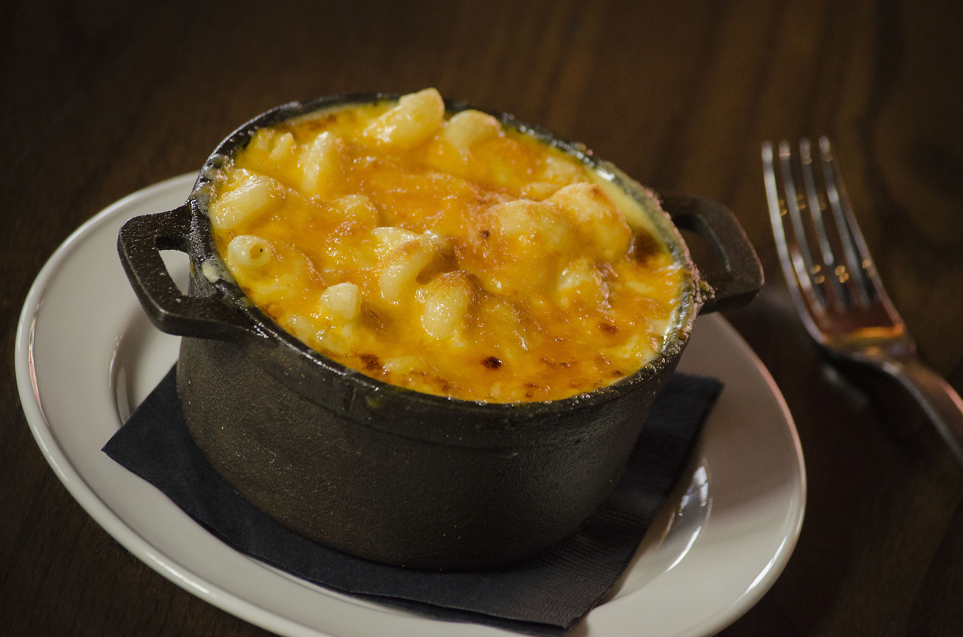 A dish of macaroni and cheese in a black cast iron pot on a white plate with a fork beside it.