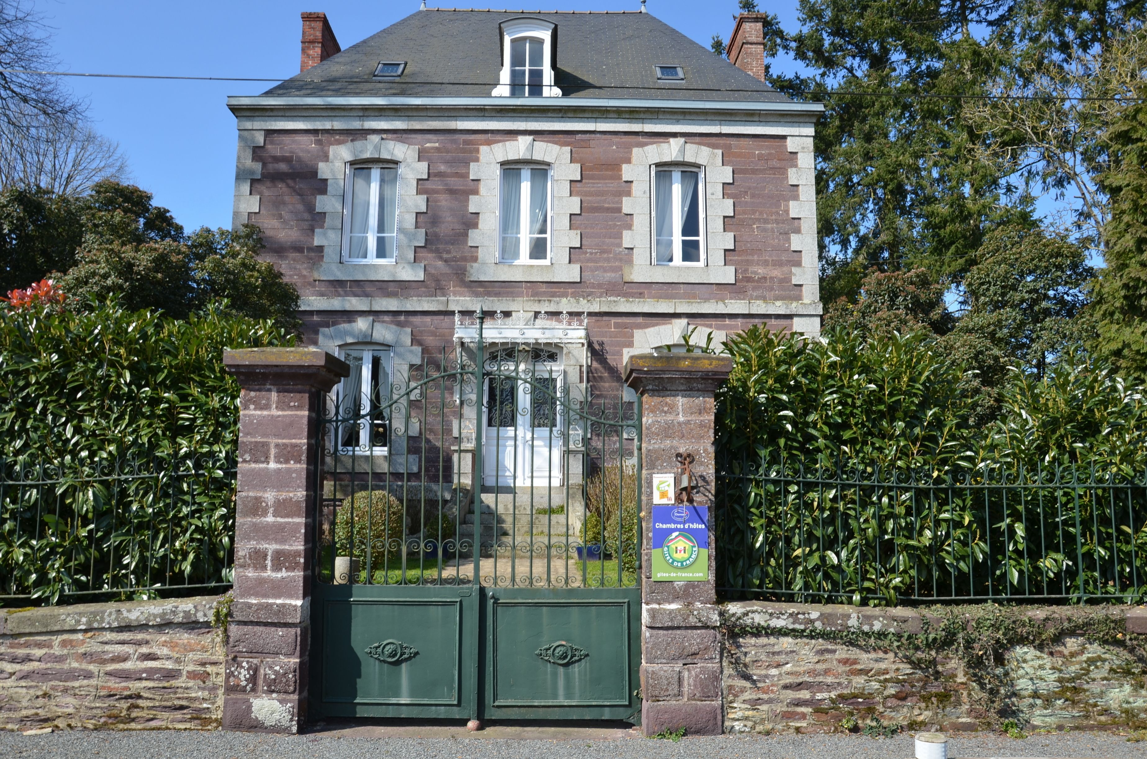 A two-story brick building with a green gate, a small balcony, and a sign indicating a chapel.
