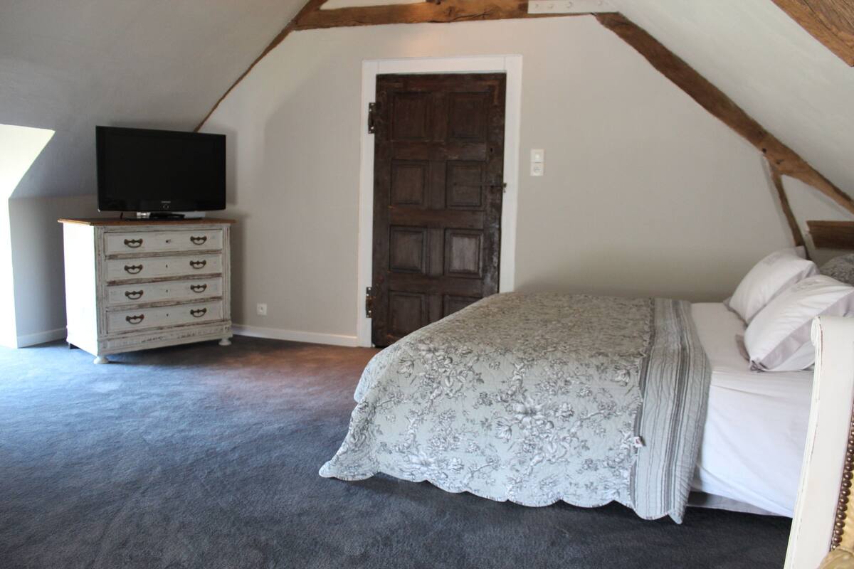 A bedroom with a bed, a dresser, and a television on a shelf.