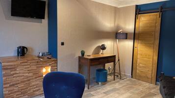 Ein modernes Wohnzimmer mit Couchtisch aus Holz, einem blauen Sessel, einem Schreibtisch mit Globus und Lampe sowie einem an der Wand befestigten Fernseher.