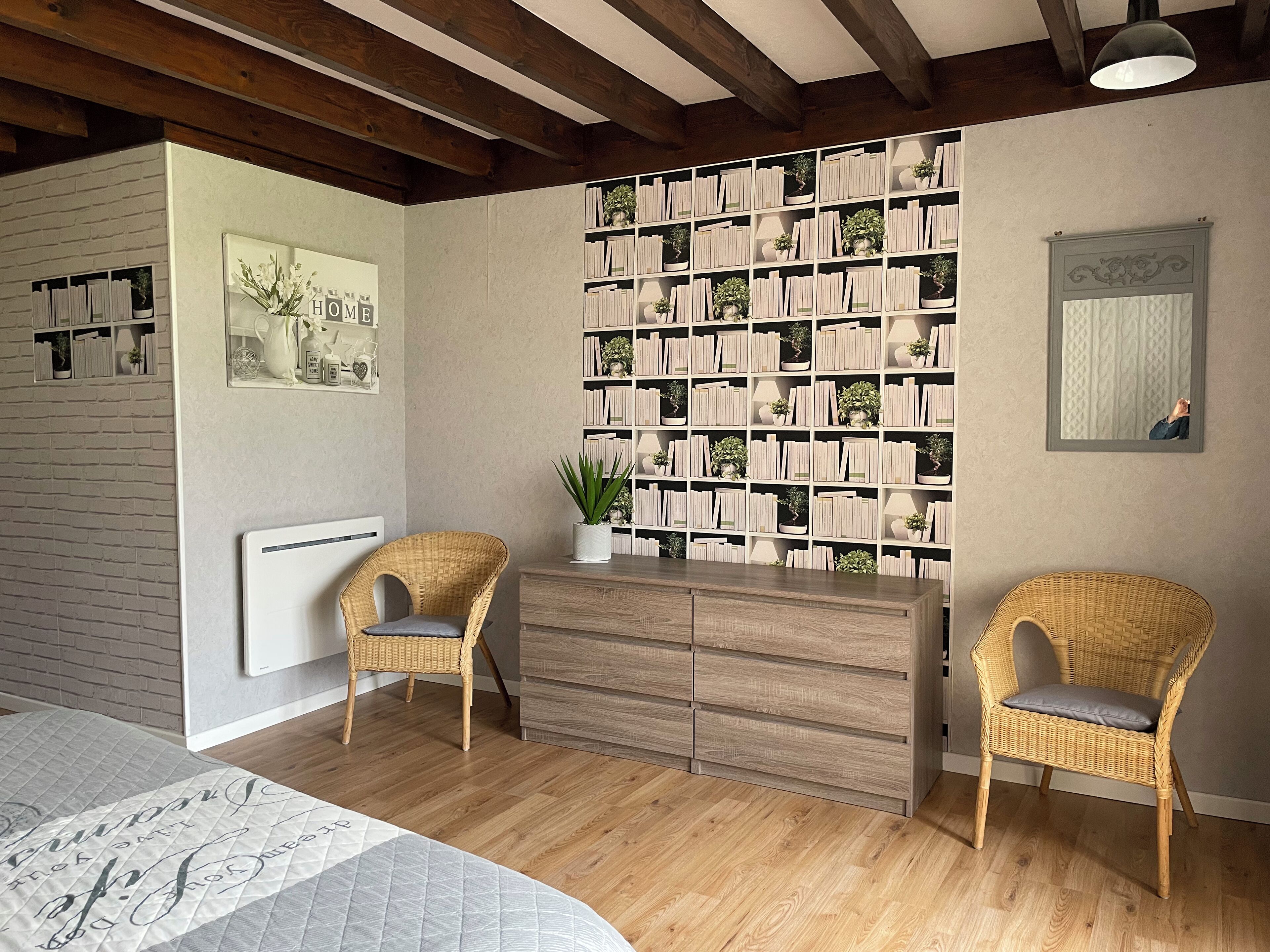A room with a large bookshelf, two wicker chairs, a wooden dresser, and a wall-mounted mirror.
