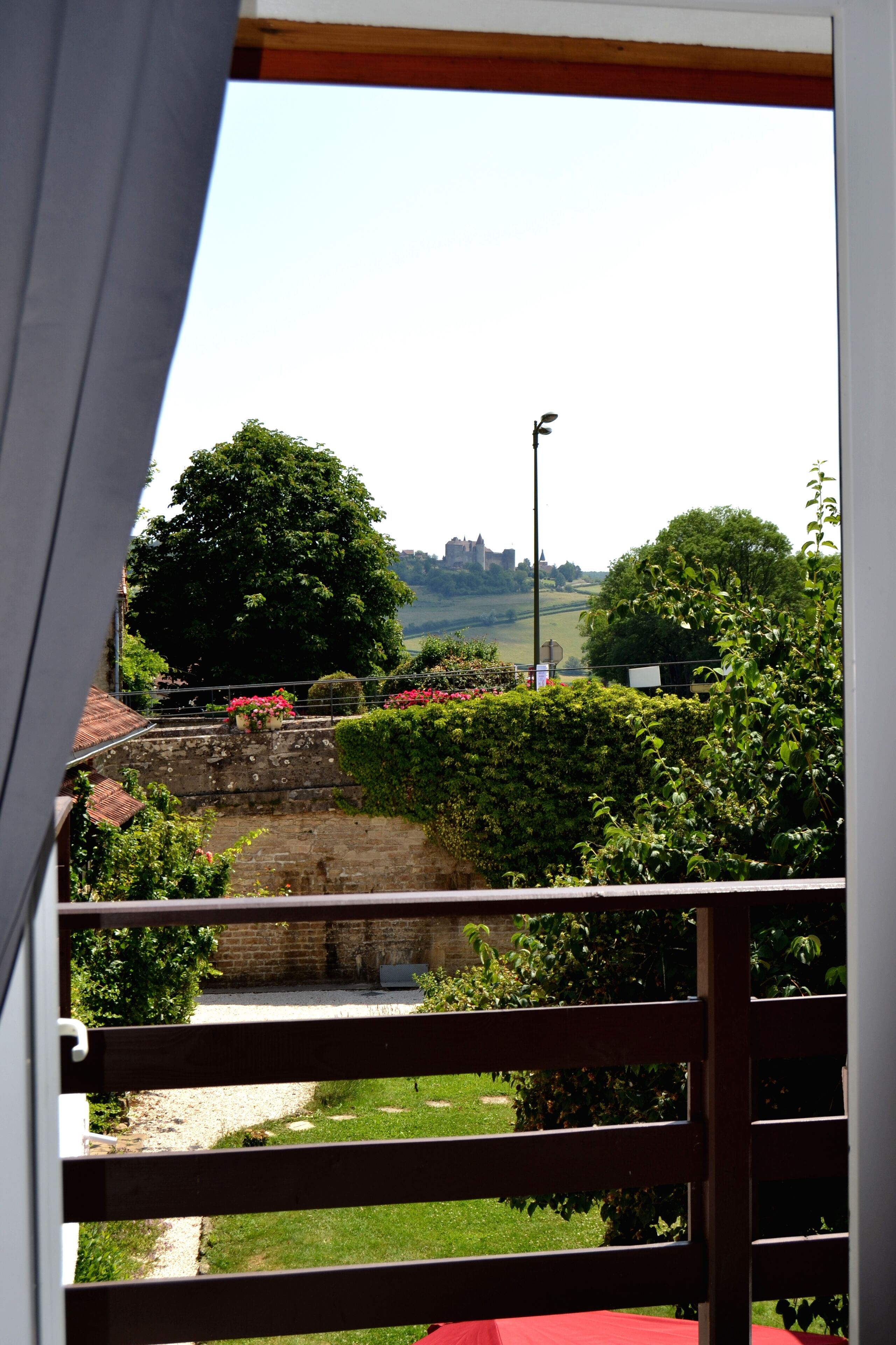 Un balcon donnant sur un mur de pierre, de la verdure et un château situé au loin.