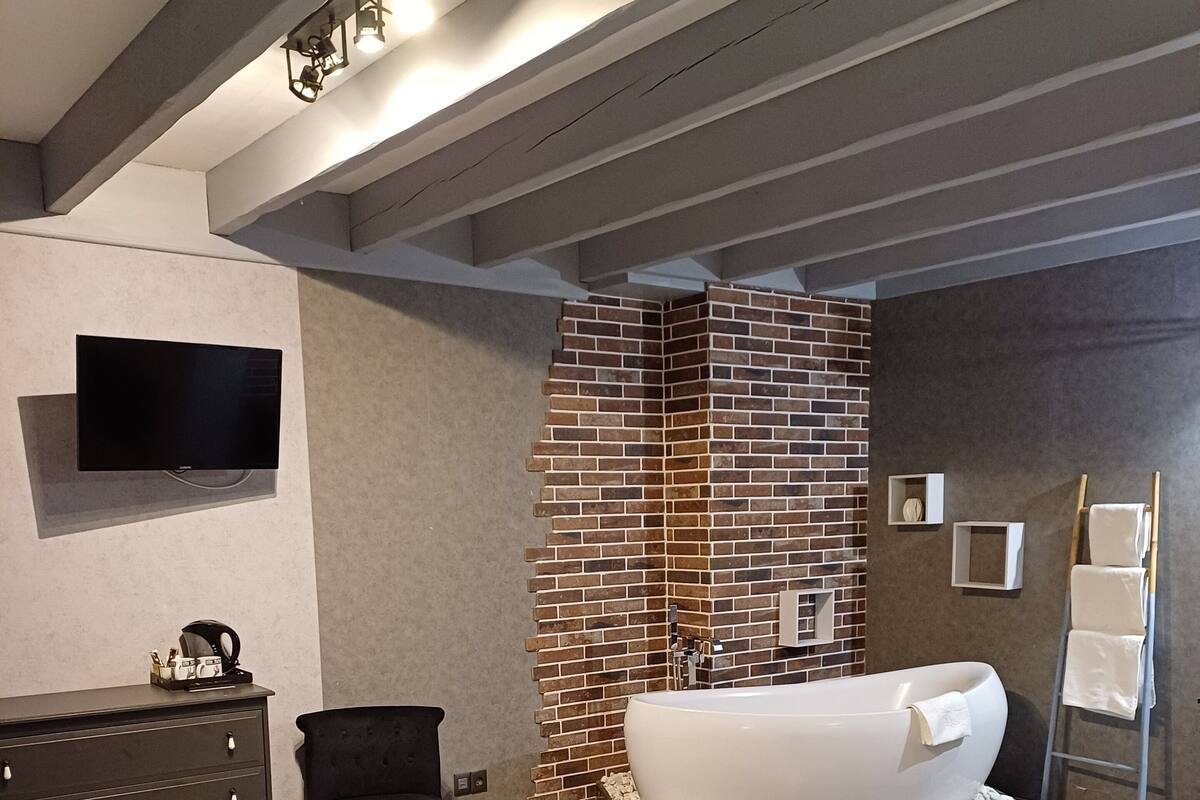 Ein modernes Schlafzimmer mit einem großen Bett, einem schwarzen Sessel, einer weißen Badewanne und einem Fernseher an der Wand.