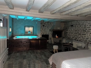 A room with a stone wall, a fireplace, a hot tub, and a bed.