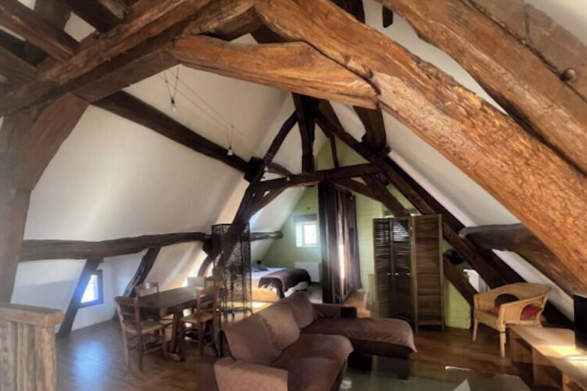 Ein rustikales Dachzimmer mit sichtbaren Holzbalken, einem Holztisch und einer Couch.