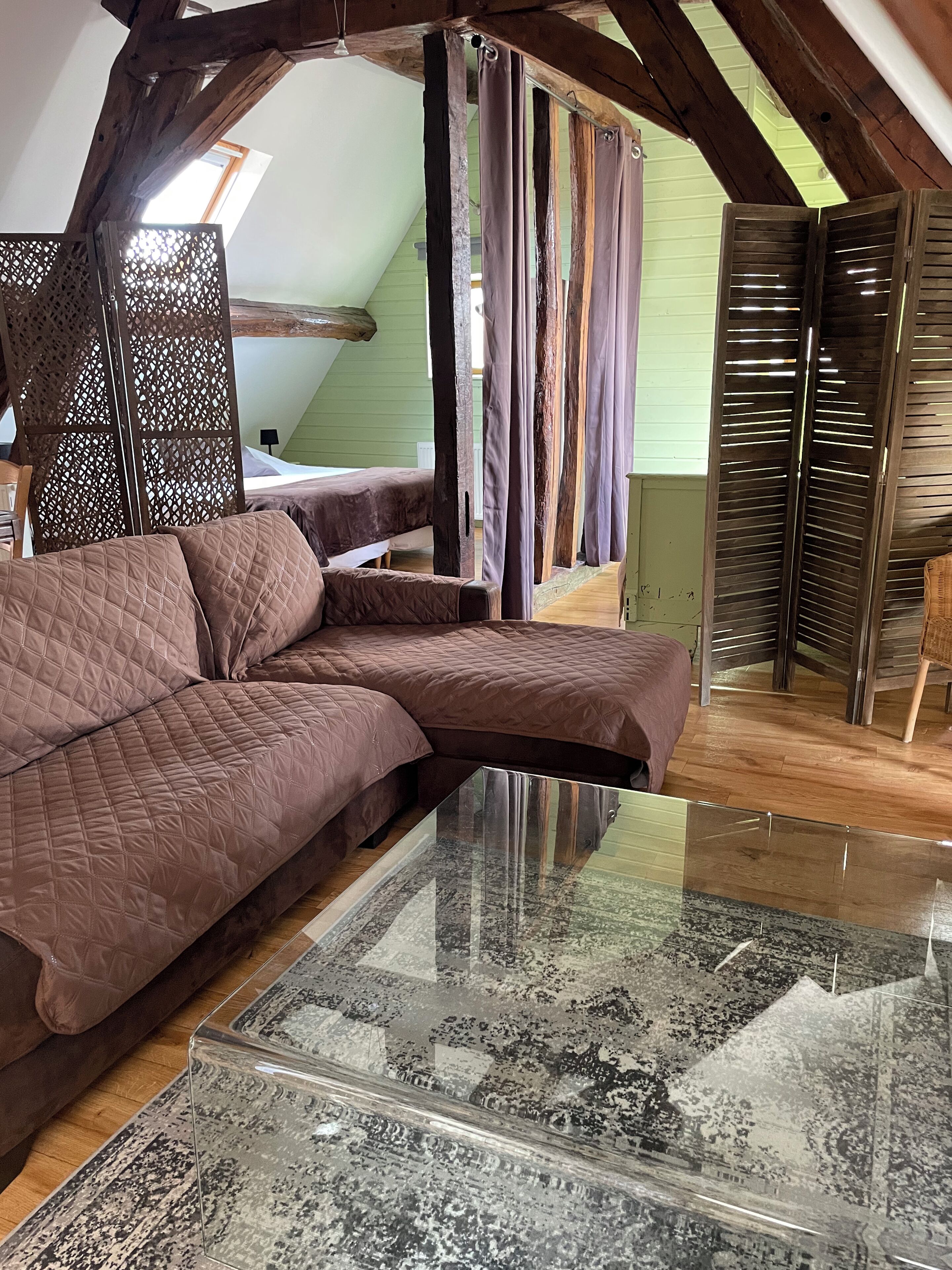 A cozy loft bedroom with a large bed, a glass coffee table, and a view of the sky through a window.