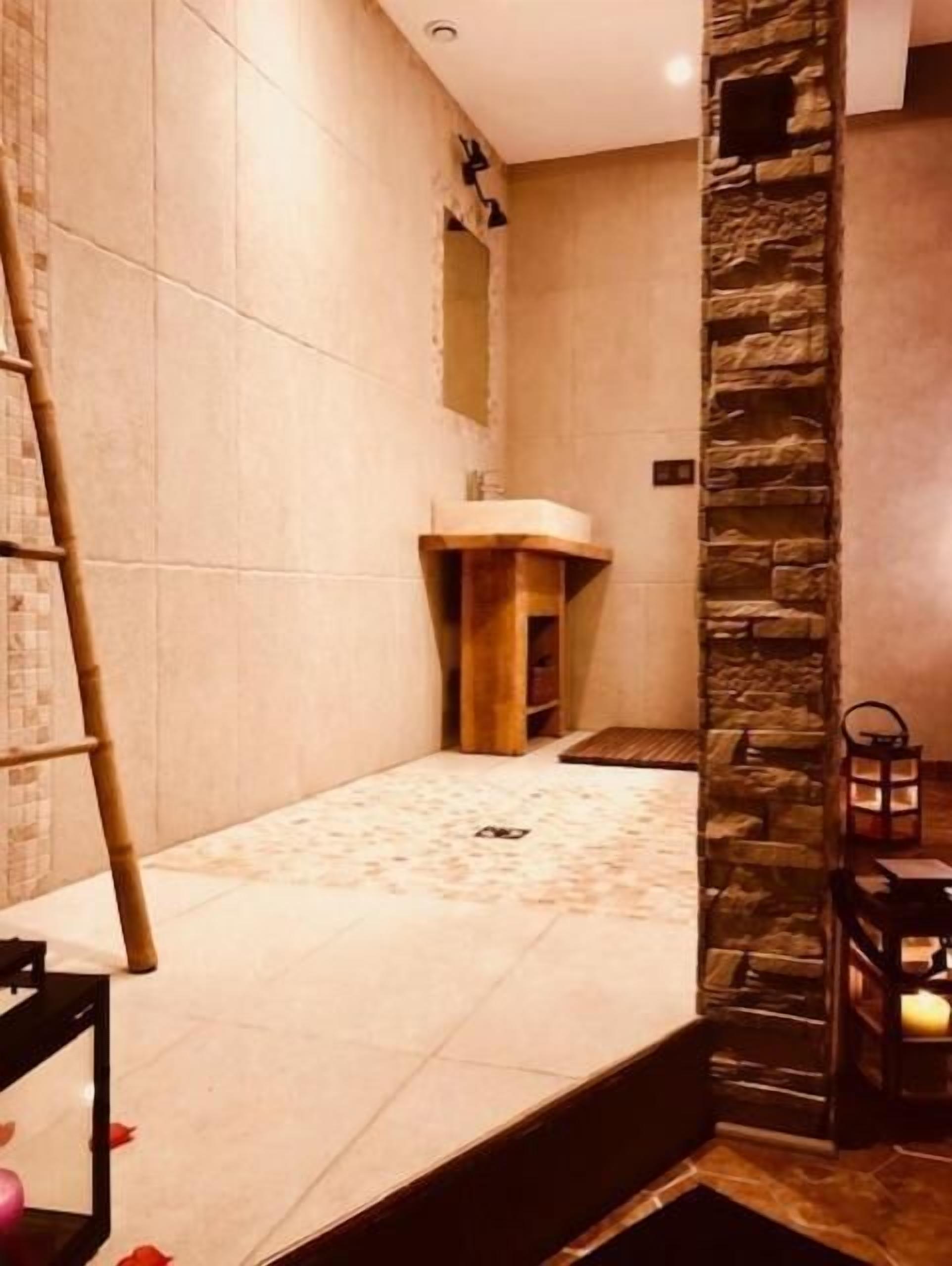 Une salle de spa avec un mur en pierre, un banc en bois et une petite table en bois sur laquelle est posée une bougie.