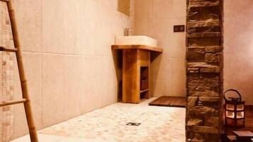 Une salle de spa avec un mur en pierre, un banc en bois et une petite table en bois sur laquelle est posée une bougie.