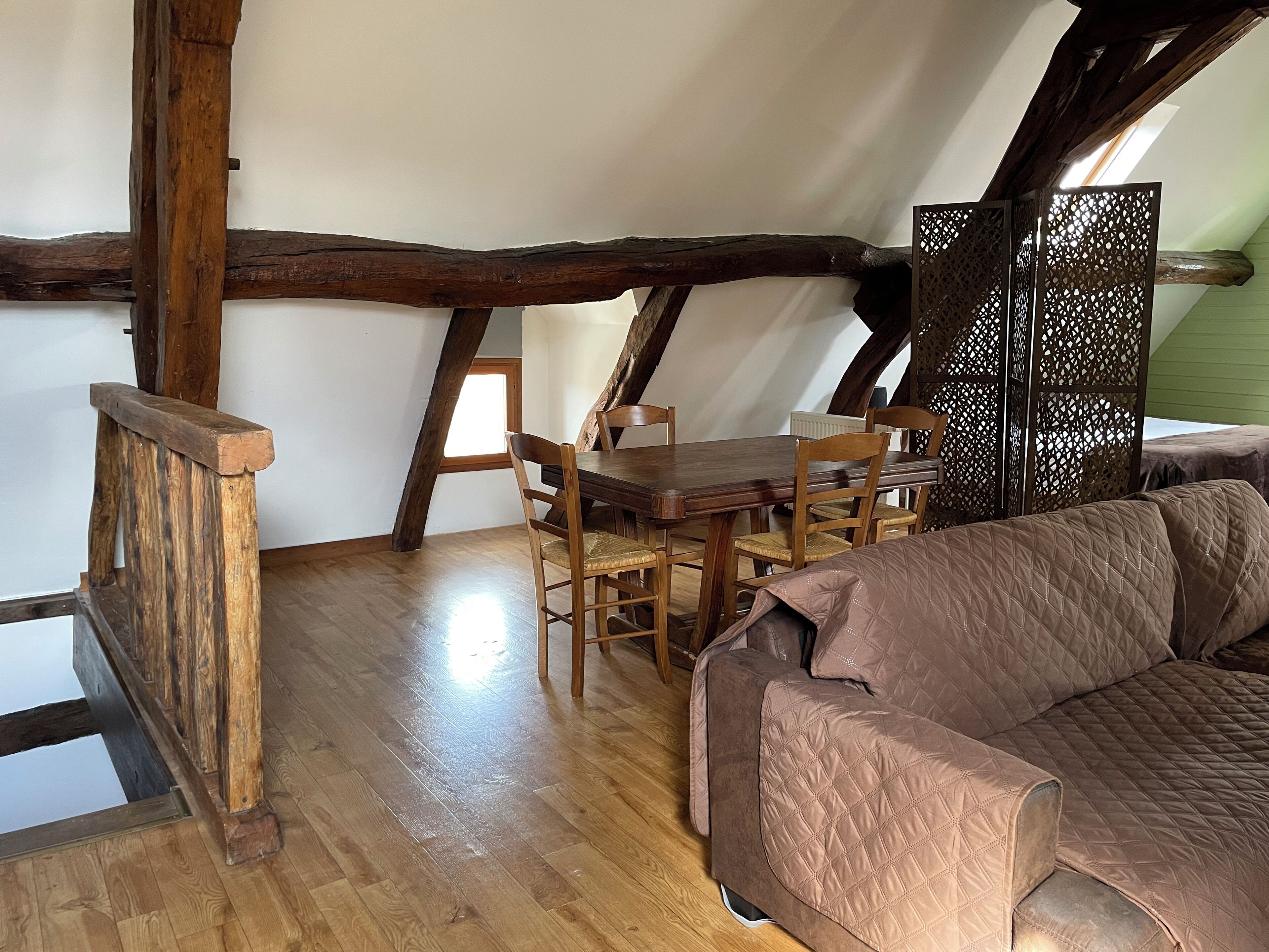 A cozy attic bedroom with a wooden ceiling, a dining table, and a cushioned sofa.