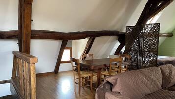 Ein gemütliches Schlafzimmer unter dem Dach mit Holzbalkendecke, einem Esstisch und einer gepolsterten Couch.