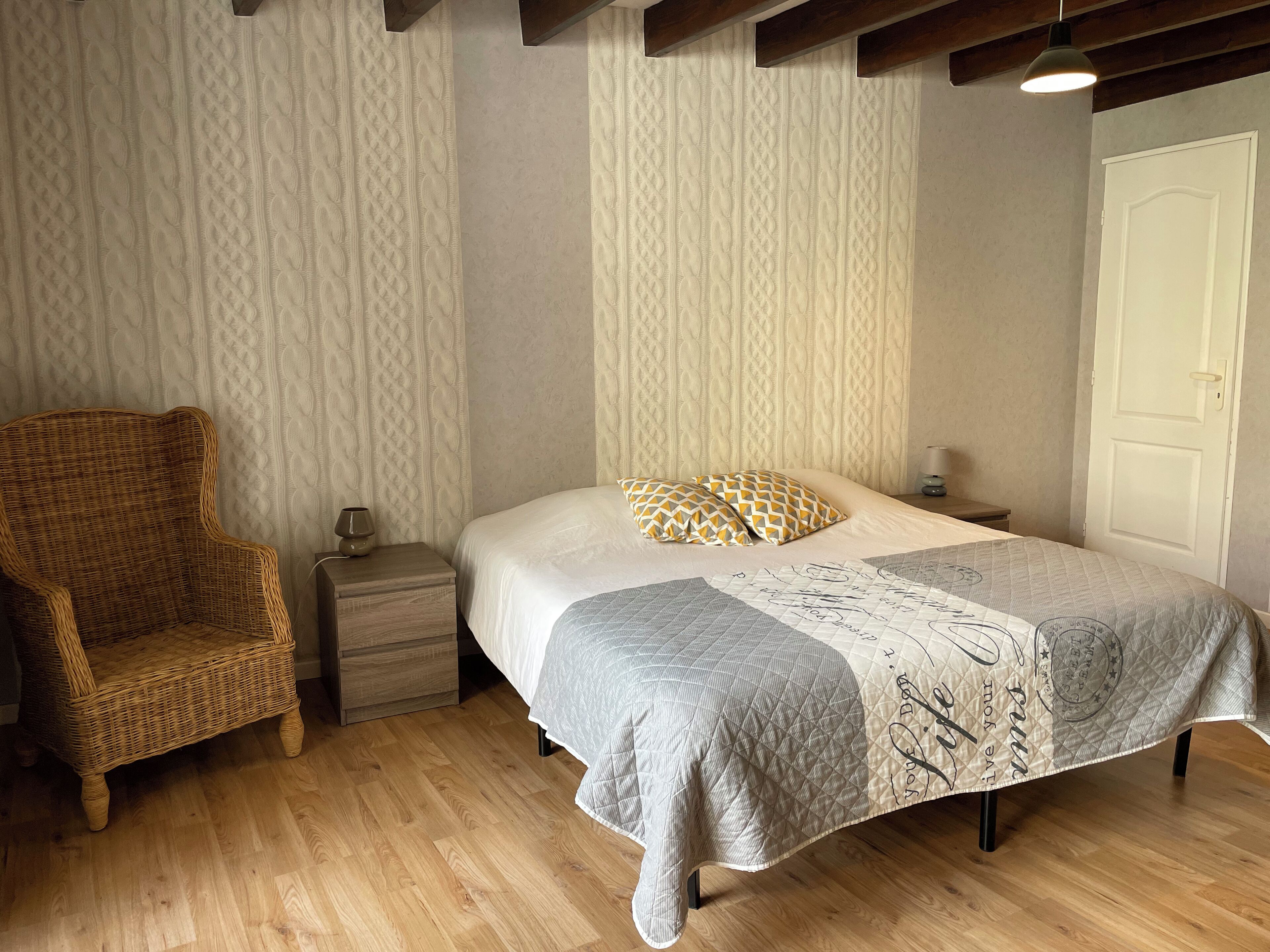 A bedroom with a bed, a nightstand, a wicker chair, and a door.