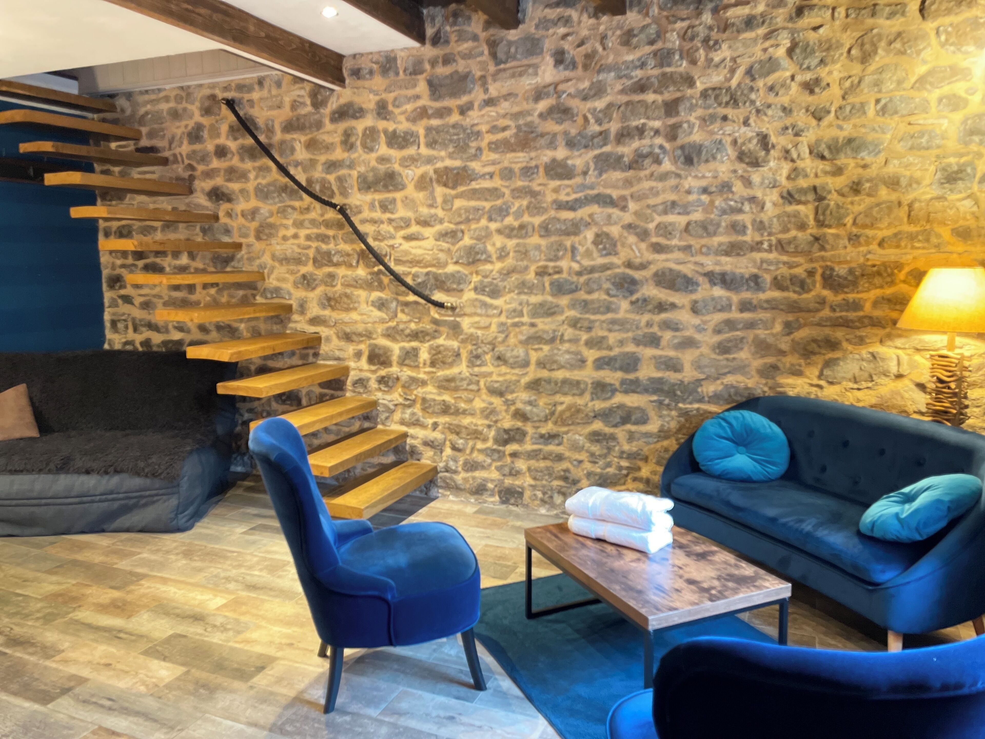 A modern living room with a stone wall, a blue sofa, a blue armchair, and a wooden coffee table.