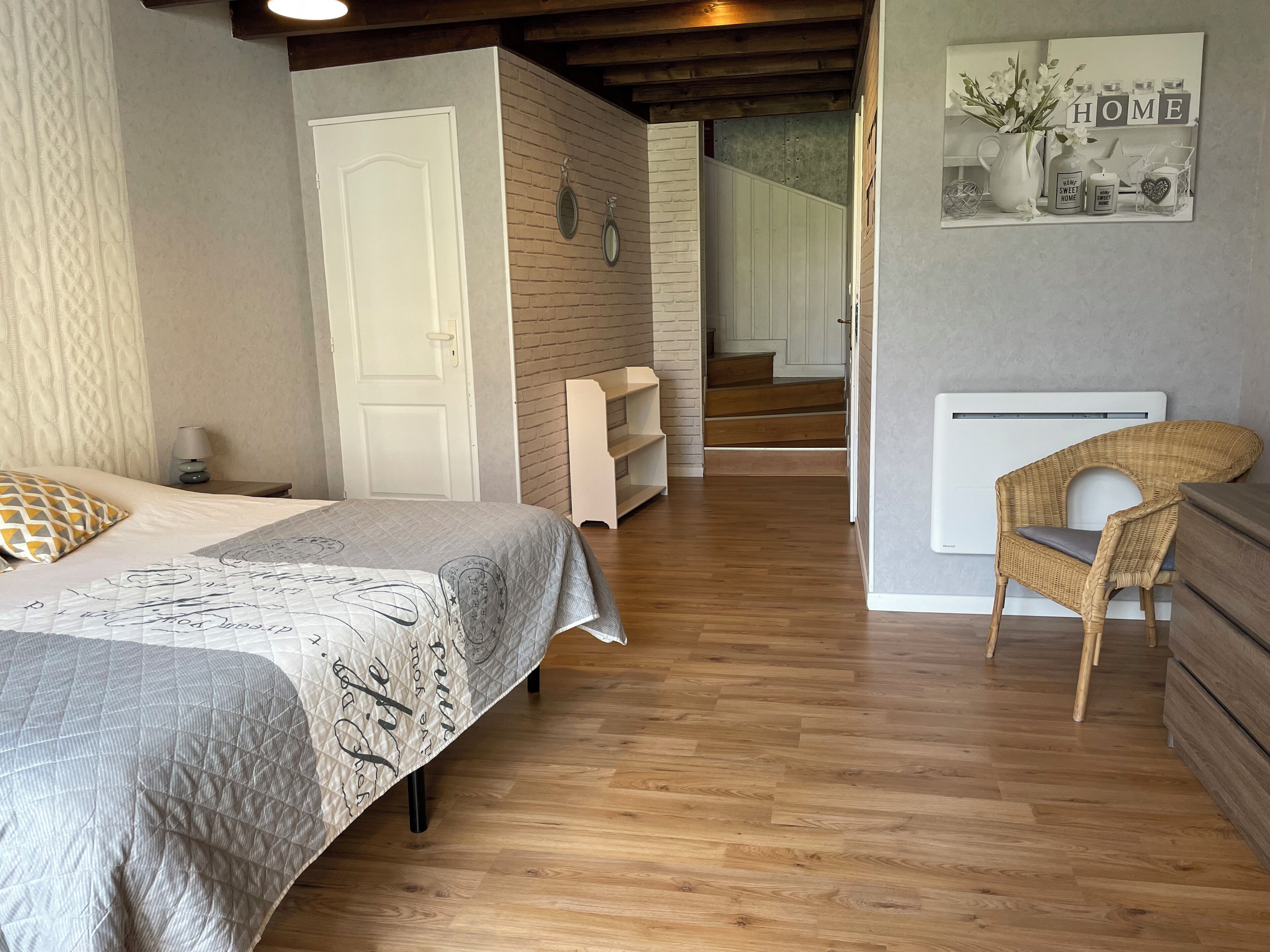 Ein Schlafzimmer mit Bett, Stuhl, Ablagefläche und einer Treppe, die in einen anderen Raum führt.